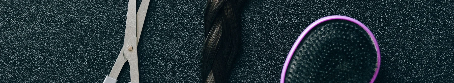Hairdressing scissors and a brush on a dark textured surface