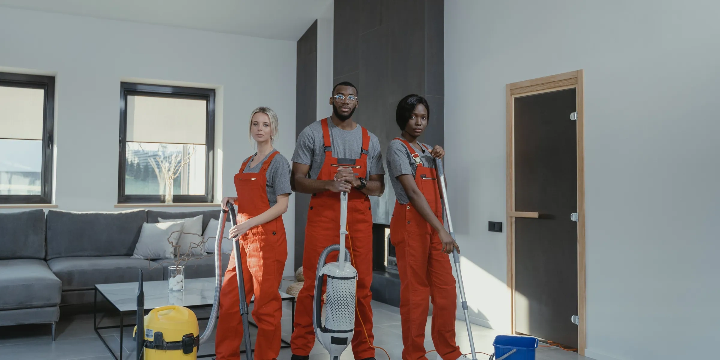 Three professional cleaners in uniform ready to clean a bright living room